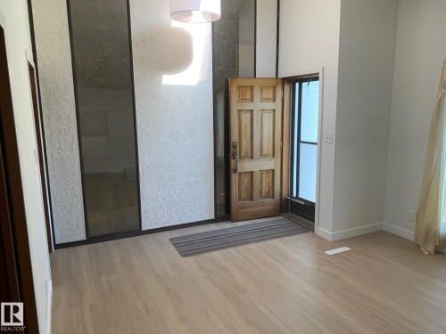 Bright entryway featuring wood-finish flooring, a textured accent wall with dark paneled inserts, and a high ceiling - 16321 - 109A Ave Nw, Edmonton, AB - Indoor