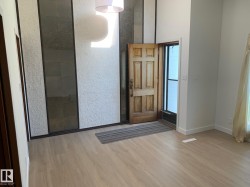 Bright entryway featuring wood-finish flooring, a textured accent wall with dark paneled inserts, and a high ceiling - 