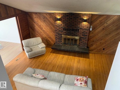 Living area featuring a brick fireplace with a brass insert, slate hearth, and two sconce light fixtures - 16321 - 109A Ave Nw, Edmonton, AB - Indoor Photo Showing Living Room With Fireplace