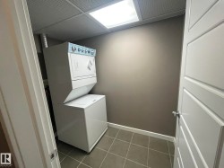 Dedicated laundry area featuring a stacked washer and dryer, square tile flooring, a drop ceiling with integrated lighting, and neutral wall paint - 