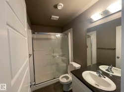 Bathroom featuring a walk-in shower with glass enclosure, white vanity with dual sinks, dark countertop, and dark floor tiles - 