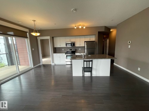 Open-concept living area featuring dark wood-finish flooring, a kitchen island with a stone-look countertop, white cabinetry, and stainless steel appliances - 504 10518 113 Street, Edmonton, AB - Indoor Photo Showing Kitchen