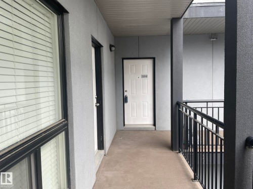 Entryway featuring a solid panel door with transom, textured exterior walls, and a black metal railing - 504 10518 113 Street, Edmonton, AB - Outdoor With Exterior