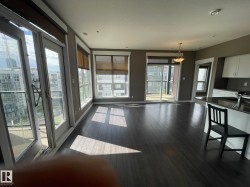 Open-concept living area with dark wood-finish flooring, multiple large windows, and direct access to a balcony - 