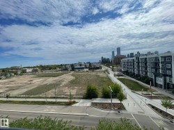 Urban landscape featuring a distant city skyline, multi-story residential buildings with balconies, paved roadways, and undeveloped land parcels - 