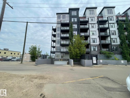 Contemporary multi-story building featuring a facade of light and dark paneling, individual balconies with glass railings, and a ground-level entrance to an underground parking facility - 504 10518 113 Street, Edmonton, AB - Outdoor With Balcony With Facade