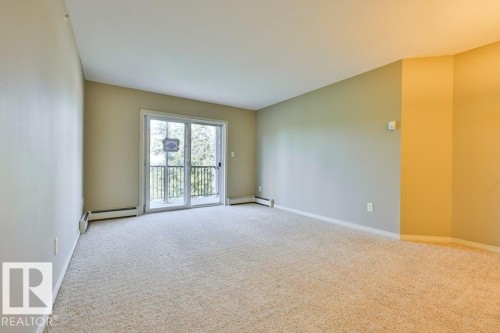 Spacious room featuring neutral carpeting, light-toned walls, and a sliding glass door leading to an outdoor balcony with metal railings - #406 4903 47 Av, Stony Plain, AB - Indoor Photo Showing Other Room
