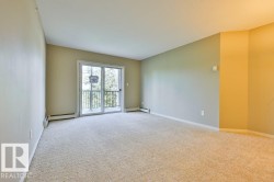 Spacious room featuring neutral carpeting, light-toned walls, and a sliding glass door leading to an outdoor balcony with metal railings - 