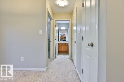 Carpeted hallway with light gray walls, white trim, and a ceiling-mounted light fixture - #406 4903 47 Av, Stony Plain, AB - Indoor Photo Showing Other Room