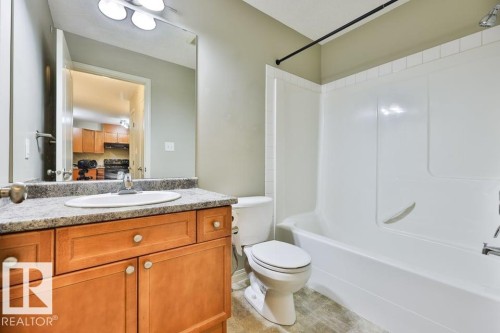 Bathroom featuring a light wood-finish vanity with a stone-finish countertop, undermount sink, and a combination shower/tub with white surround - #406 4903 47 Av, Stony Plain, AB - Indoor Photo Showing Bathroom