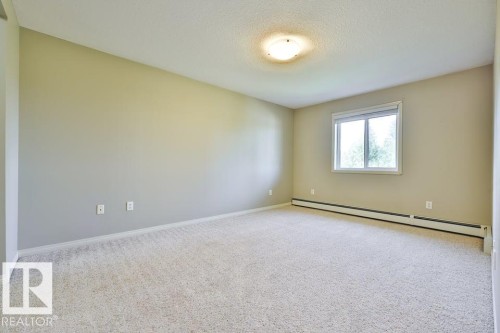 Spacious interior room featuring light-colored carpet flooring, neutral wall paint, and a textured ceiling - #406 4903 47 Av, Stony Plain, AB - Indoor Photo Showing Other Room