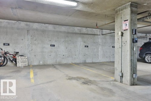 Underground parking space featuring concrete walls and ceiling, painted concrete flooring, and overhead fluorescent lighting - #406 4903 47 Av, Stony Plain, AB - Indoor Photo Showing Garage