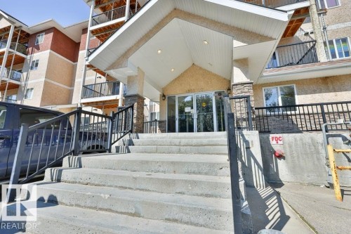 Building entrance featuring concrete stairs with black metal railings, a covered entry with recessed lighting, and a glass double door - #406 4903 47 Av, Stony Plain, AB - Outdoor