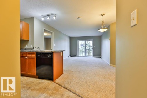 Kitchen with wood cabinetry and dark countertops, integrated with a carpeted living area featuring a sliding glass door to an exterior balcony - #406 4903 47 Av, Stony Plain, AB - Indoor