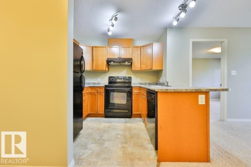 U-shaped kitchen with wood cabinetry and black appliances, complemented by a light-toned countertop - #406 4903 47 Av, Stony Plain, AB - Indoor Photo Showing Kitchen