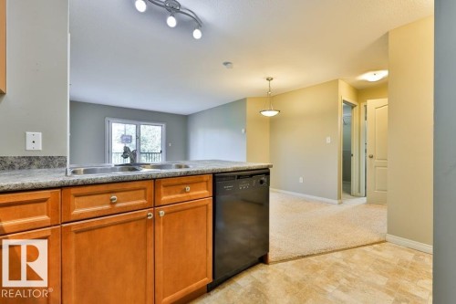 Kitchen bar with wood cabinetry, integrated dishwasher, and double basin sink - #406 4903 47 Av, Stony Plain, AB - Indoor Photo Showing Kitchen With Double Sink
