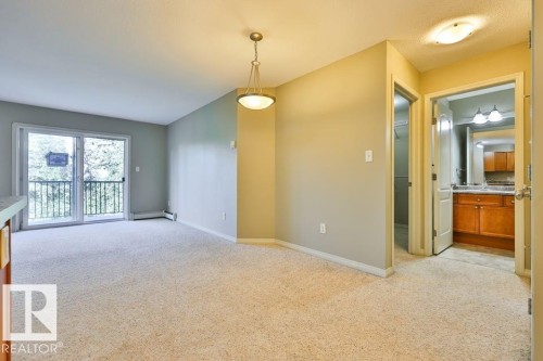 Open-concept living area featuring light-toned carpeting, a sliding glass door with balcony access, and a contemporary pendant light fixture - #406 4903 47 Av, Stony Plain, AB - Indoor Photo Showing Other Room