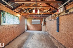 Open garage space featuring concrete flooring and exposed wood ceiling rafters - 