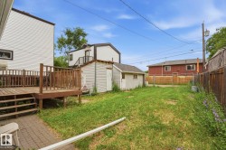 Expansive grassy yard featuring a multi-level wood deck, a paved patio section, and a standalone storage shed - 