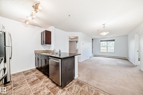 Kitchen area featuring dark wood-finish cabinetry, stainless steel appliances, and a double basin sink with a chrome faucet - 103 3315 James Mowatt Trail Sw, Edmonton, AB - Indoor Photo Showing Kitchen With Double Sink