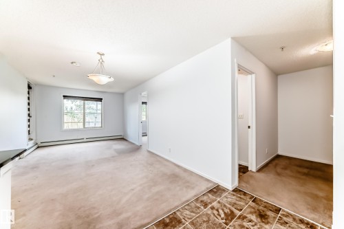 Bright room featuring a large window, a classic ceiling light fixture, and neutral carpeting - 103 3315 James Mowatt Trail Sw, Edmonton, AB - Indoor Photo Showing Other Room