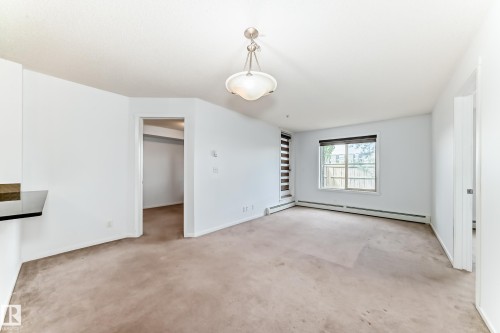 Open-concept room featuring neutral carpeting, white walls, and a contemporary ceiling light fixture - 103 3315 James Mowatt Trail Sw, Edmonton, AB - Indoor Photo Showing Other Room