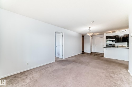 Open-concept living area featuring a kitchen with dark cabinetry and stainless steel appliances - 103 3315 James Mowatt Trail Sw, Edmonton, AB - Indoor
