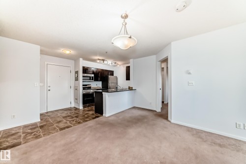 Open-concept living area featuring a kitchen with dark cabinetry, stainless steel appliances, and a breakfast bar - 103 3315 James Mowatt Trail Sw, Edmonton, AB - Indoor Photo Showing Kitchen