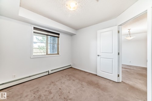 Carpeted interior room featuring a window with blinds, white trim, baseboard heating, and a textured ceiling with a flush-mount light fixture - 103 3315 James Mowatt Trail Sw, Edmonton, AB - Indoor Photo Showing Other Room