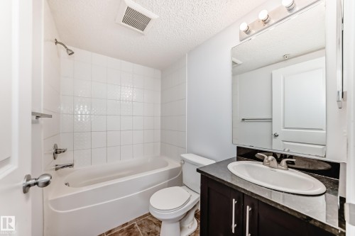 Full bathroom featuring a white tub/shower combination with subway tile surround, a dark wood-finish vanity with a built-in sink, a dark countertop, and a large wall-mounted mirror - 103 3315 James Mowatt Trail Sw, Edmonton, AB - Indoor Photo Showing Bathroom