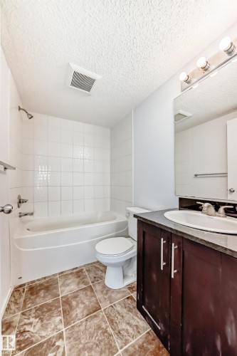 Bathroom featuring a white tub with shower, white tiled surround, and white toilet - 103 3315 James Mowatt Trail Sw, Edmonton, AB - Indoor Photo Showing Bathroom