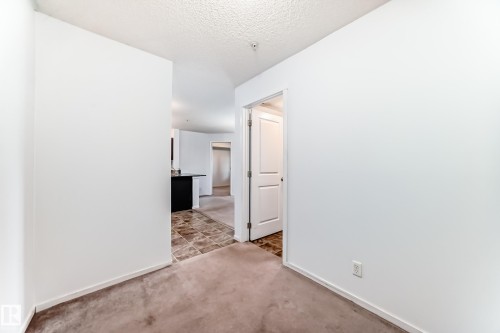 Interior room featuring a neutral carpet flooring, white walls, and a textured ceiling - 103 3315 James Mowatt Trail Sw, Edmonton, AB - Indoor Photo Showing Other Room