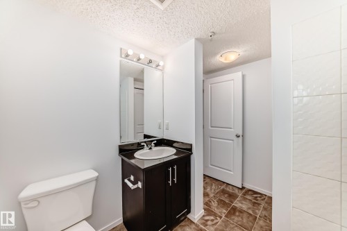 Bathroom featuring a dark wood vanity with a black countertop, oval undermount sink, and chrome faucet - 103 3315 James Mowatt Trail Sw, Edmonton, AB - Indoor Photo Showing Bathroom