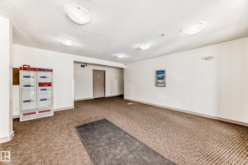 Carpeted entryway with multi-unit mailboxes and flush-mount ceiling lighting - 103 3315 James Mowatt Trail Sw, Edmonton, AB - Indoor Photo Showing Other Room