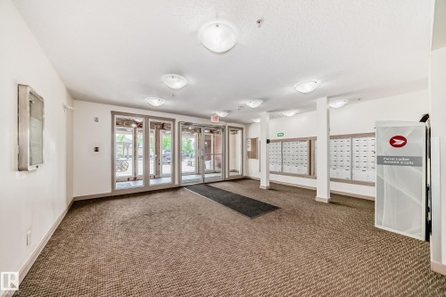 Inviting entryway featuring glass-paneled double doors, durable carpet flooring, overhead dome lighting, and built-in mailboxes - 103 3315 James Mowatt Trail Sw, Edmonton, AB - Indoor Photo Showing Other Room