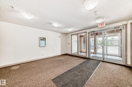 Building entry with glass doors and sidelights, featuring a textured carpet flooring and flush-mount ceiling lights - 103 3315 James Mowatt Trail Sw, Edmonton, AB - Indoor Photo Showing Other Room