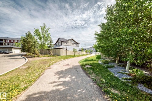 Paved pathway bordered by mature trees and established landscaping - 103 3315 James Mowatt Trail Sw, Edmonton, AB - Outdoor
