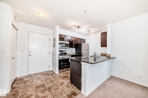 Kitchen area featuring dark wood-finish cabinetry, stainless steel appliances, and a dark countertop - 103 3315 James Mowatt Trail Sw, Edmonton, AB - Indoor Photo Showing Kitchen