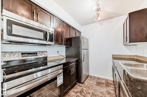 Kitchen featuring stainless steel appliances including a refrigerator, microwave, and range - 103 3315 James Mowatt Trail Sw, Edmonton, AB - Indoor Photo Showing Kitchen With Double Sink