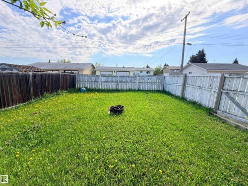 Expansive backyard featuring a green lawn, wood fence perimeter, and a fire pit - 4823 49 Street, Clyde, AB - Outdoor