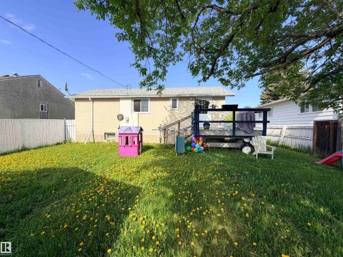 Expansive backyard featuring green lawn, mature trees, and a raised wooden deck with railings - 4823 49 Street, Clyde, AB - Outdoor With Deck Patio Veranda