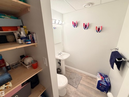 Compact bathroom featuring a pedestal sink, a toilet, a vanity light fixture, and wood-finish flooring - 4823 49 Street, Clyde, AB - Indoor Photo Showing Bathroom