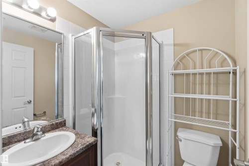 Bathroom featuring a glass-enclosed shower, a vanity with a white oval sink, a patterned countertop, a wall-mounted mirror, and a toilet - #708 9939 109 St Nw, Edmonton, AB - Indoor Photo Showing Bathroom