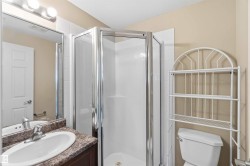 Bathroom featuring a glass-enclosed shower, a vanity with a white oval sink, a patterned countertop, a wall-mounted mirror, and a toilet - 