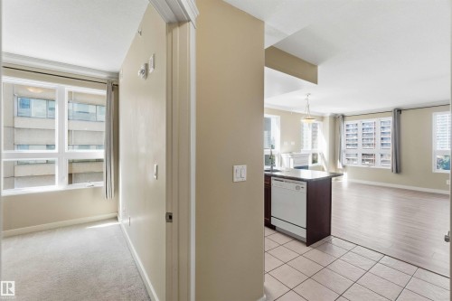 Open-concept living space featuring a kitchen island with integrated dishwasher, tile flooring, and light wood-finish flooring - #708 9939 109 St Nw, Edmonton, AB - Indoor