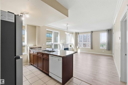 Open-concept living area featuring a kitchen island with a double basin sink and dark wood cabinetry - #708 9939 109 St Nw, Edmonton, AB - Indoor Photo Showing Kitchen With Double Sink