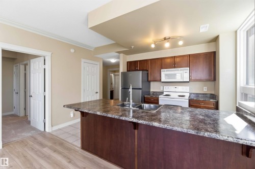 Kitchen featuring a dual basin sink, stainless steel refrigerator, white range, and built-in microwave - #708 9939 109 St Nw, Edmonton, AB - Indoor Photo Showing Kitchen With Double Sink