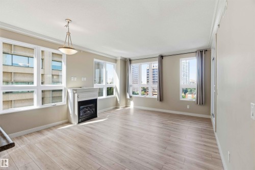 Bright living space featuring expansive windows, wood-finish flooring, a decorative fireplace with a classic mantel, and an overhead pendant light fixture - #708 9939 109 St Nw, Edmonton, AB - Indoor Photo Showing Living Room With Fireplace