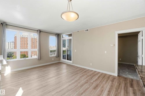 Bright room featuring wood-finish flooring, multiple windows, a sliding glass door, crown molding, and a built-in ceiling light fixture - #708 9939 109 St Nw, Edmonton, AB - Indoor Photo Showing Other Room