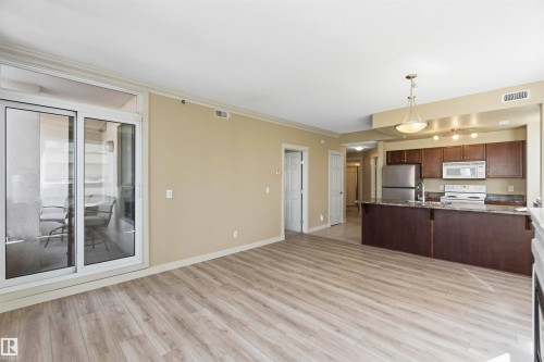 Open-concept living space featuring wood-finish flooring, a kitchen island with seating, a full suite of stainless steel appliances, and a sliding glass door leading to a balcony - #708 9939 109 St Nw, Edmonton, AB - Indoor Photo Showing Kitchen